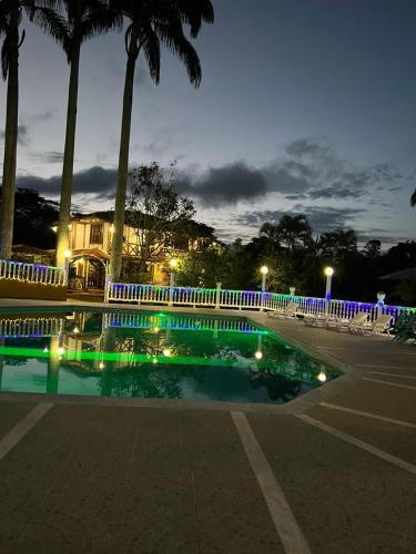 a swimming pool at night with a white fence and palm trees at Hotel campestre los Arrieros in Guaduas
