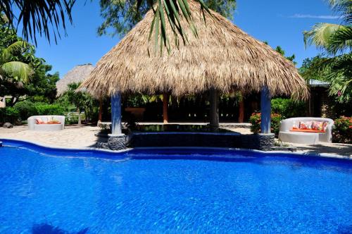 a resort swimming pool with a straw hut at Surf Sanctuary in El Limón