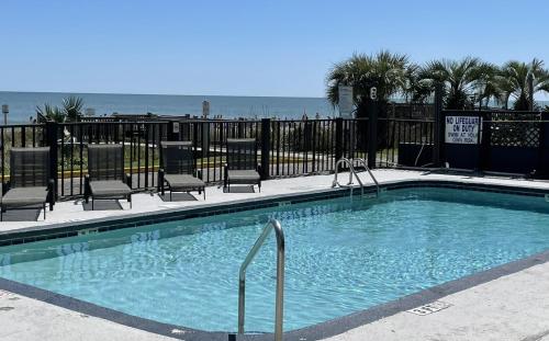 a swimming pool with chairs and the ocean in the background at Blue Palmetto in Myrtle Beach