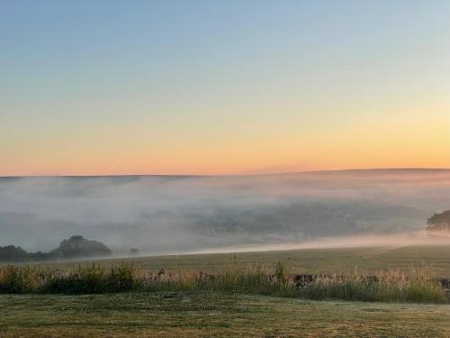 a foggy field with the sun setting in the background at Oakley View Shepherds Hut with hot tub in Whitby