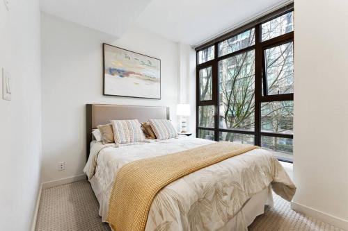 a white bedroom with a bed and a window at Fabulous 2Bdr Duplex in Yaletown in Vancouver