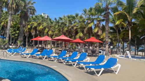 a row of blue chairs and red umbrellas next to a pool at Punta Centinella Yacht Club in Santa Elena
