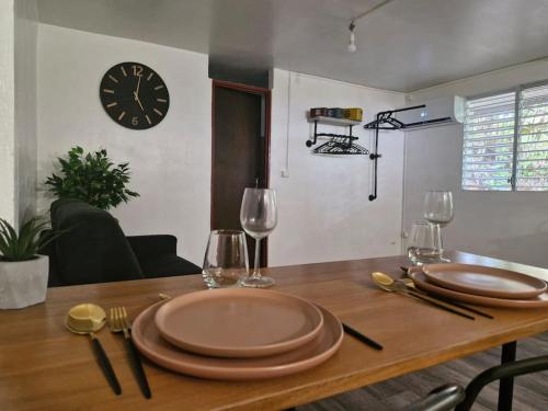 uma mesa com pratos e copos de vinho e um relógio em Le Vénusien em Le Robert