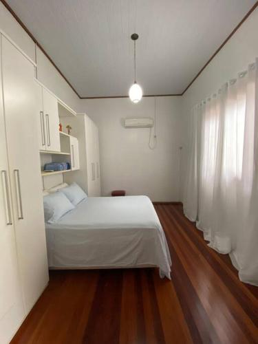 a bedroom with a white bed and a wooden floor at Quarto casa Guaporé in Guaporé