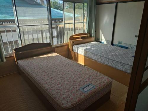 a room with two beds and a balcony with windows at 名高儀の宿 in Iwaki