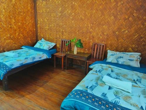 two beds in a room with a table and two chairs at Lokal Hut Bed and Breakfast in Puerto Princesa City