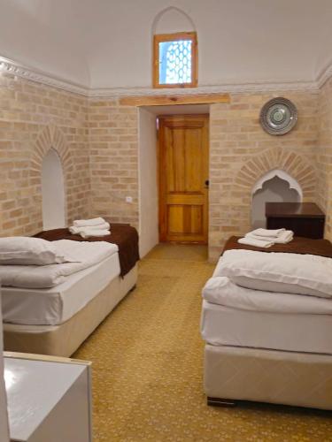 a bedroom with two beds and a wooden door at Orient Star Khiva Hotel- Madrasah Muhammad Aminkhan 1855 in Khiva