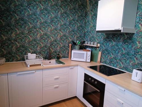 une cuisine avec des armoires blanches, un évier et un micro-ondes dans l'établissement Maison Salomé en hyper centre (intégralement rénovée et équipée), à Saint-Omer