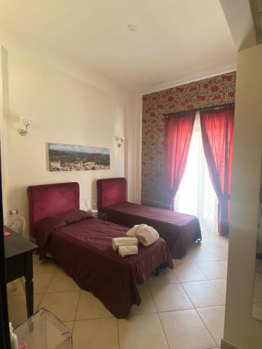 a bedroom with two beds and a window with red curtains at Regalpetra Hotel in Racalmuto