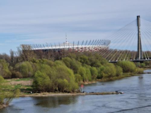 a bridge over a river with a stadium in the background at Przy moście pieszo-rowerowym BETTER PLACE Port Praski Loft in Warsaw