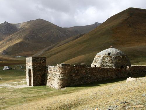 ein altes Steingebäude auf einem Feld mit Bergen im Hintergrund in der Unterkunft Mikasa Guest House in Naryn