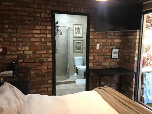 ein Schlafzimmer mit einer Ziegelwand und ein Badezimmer mit einer Dusche in der Unterkunft Aloe Klerksdorp in Klerksdorp