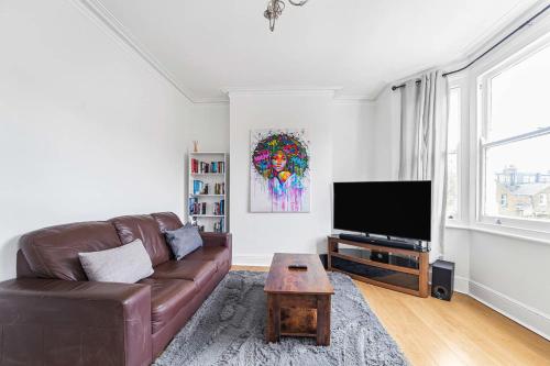 a living room with a brown leather couch and a tv at Bright West Ealing Abode in Hanwell