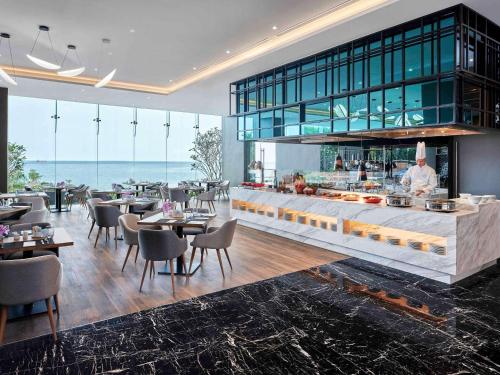 a restaurant with a counter with tables and chairs at Novotel Marina Sriracha in Si Racha