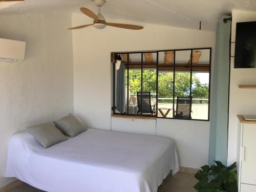 - une chambre avec un lit, un ventilateur de plafond et une fenêtre dans l'établissement Studio le Nid, vue mer, village et collines avec terrasse, à Bormes-les-Mimosas