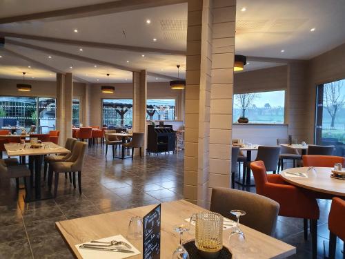 uma sala de jantar com mesas, cadeiras e janelas em Le Domaine du Cerf Blanc em Carentoir