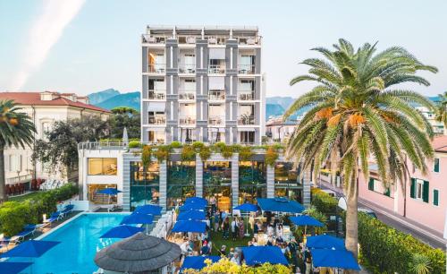 a hotel with a pool and palm trees and blue umbrellas at Hotel Excelsior in Marina di Massa