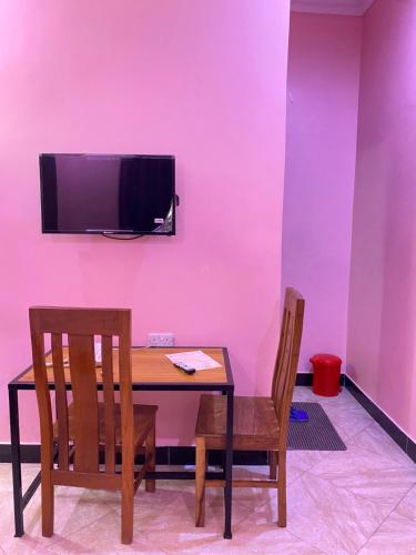 une table avec deux chaises et une télévision sur un mur rose dans l'établissement Sanic Lodge, à Dar es Salaam