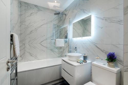 a white bathroom with a tub and a toilet and a sink at Modern Comfort Two Bedrooms Flat, Coulsdon CR5 in Coulsdon