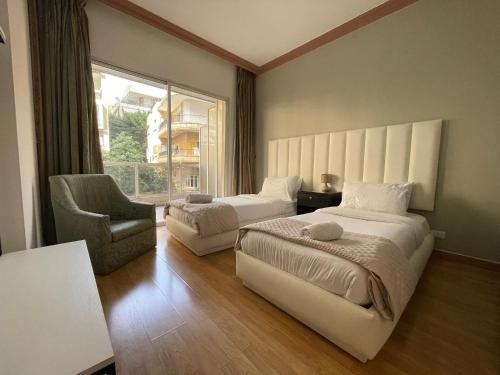 a bedroom with two beds and a chair and a window at Elegant Suites Beirut in Beirut