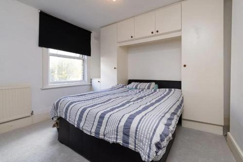 ein Schlafzimmer mit einem Bett mit gestreifter Decke und einem Fenster in der Unterkunft 2 Bed Maisonette with free parking. South Norwood in Norwood