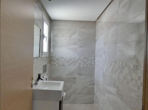 La salle de bains blanche est pourvue d'un lavabo et d'un miroir. dans l'établissement Maison LIANE familiale au calme, à Hammamet