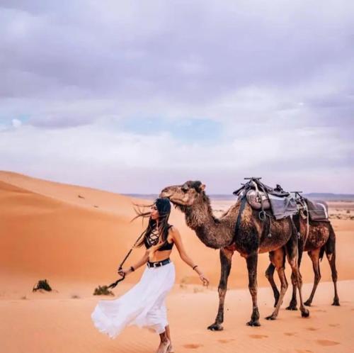 a woman walking in the desert with two camels at Merzouga Luxurious Camp in Merzouga