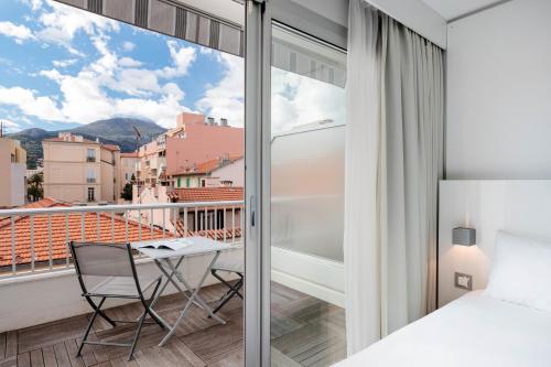 a bedroom with a balcony with a bed and a desk at Ibis Styles Menton Centre in Menton