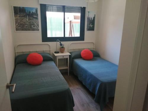2 Betten mit roten Kissen in einem kleinen Zimmer in der Unterkunft Ribera del Guadalquivir in Camas