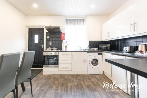 a kitchen with white cabinets and a washer and dryer at Melrose Contractor Accommodation in Manchester