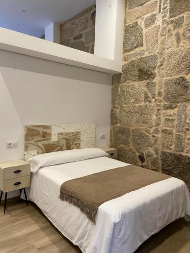 1 dormitorio con cama y pared de piedra en Reginita Apartamentos, en Arbo