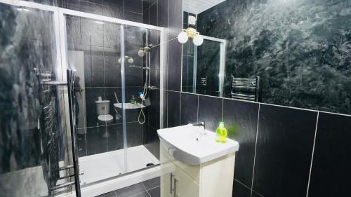 baño de azulejos negros con lavabo y ducha en F3 Ground floor Luxury flat Gants Hill, en Redbridge