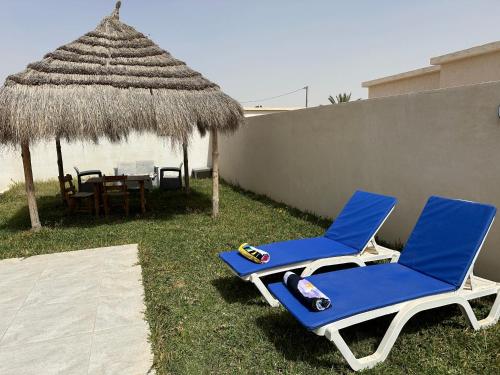 dos sillas azules y una mesa y una sombrilla de paja en Superbe villa avec piscine sans aucun vis à vis, en Djerba