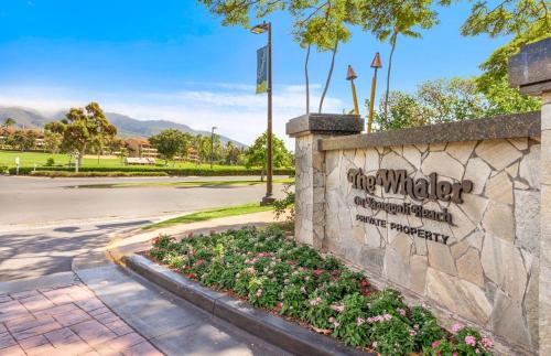 a sign on a stone wall with flowers at The Whaler By Maui Resort Rentals in Lahaina