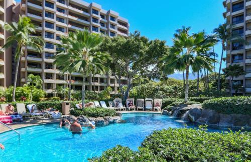 a pool at a resort with palm trees and chairs at The Kaanapali Alii By Maui Resort Rentals in Lahaina