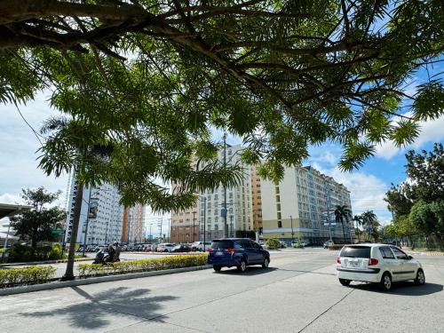two cars driving down a city street with buildings at K&K The Modern Crib at Holland Park Condo Southwoods City in Biñan