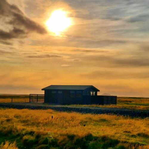 a house in the middle of a field with the sunset at Green Farm Stay with private hot tub in Hvolsvöllur