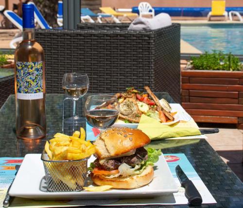 a sandwich and french fries on a table with a bottle of wine at Camping Le Luberon in Apt