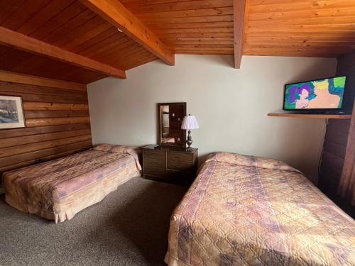 two beds in a room with a tv on the wall at Raccoon Lodge Motel in Sylvan Lake