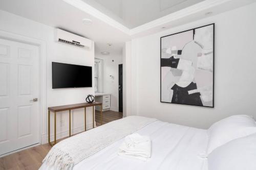 a white bedroom with a bed and a flat screen tv at Penfield Suites in Montréal