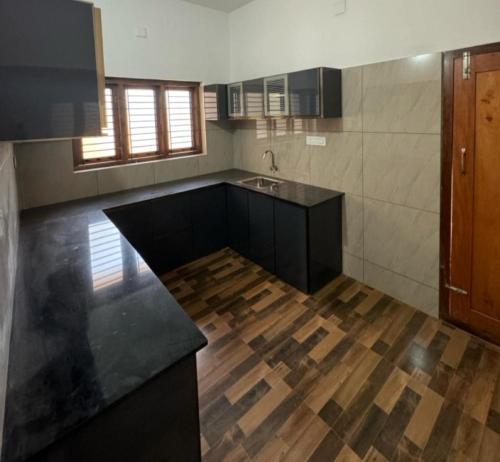 cocina con encimeras negras y suelo de madera en Oasia homestay, en Chāvasseri