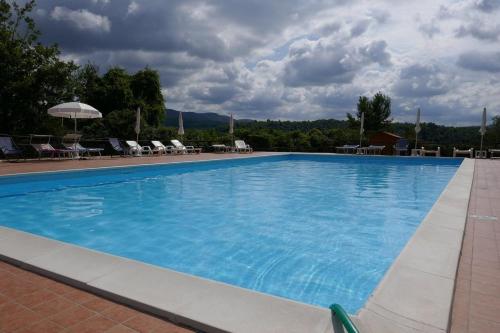 a large blue swimming pool with chairs and an umbrella at Agriturismo Casal Cerqueto in Canalicchio