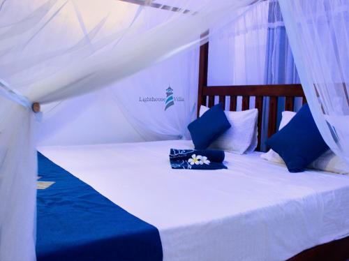 Cama blanca con almohadas azules y dosel en Lighthouse Villa Koggala, en Galle
