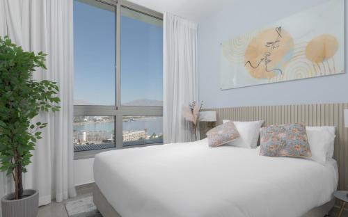 ein weißes Bett in einem Zimmer mit einem großen Fenster in der Unterkunft Nathan's Suites On The Beach in Eilat