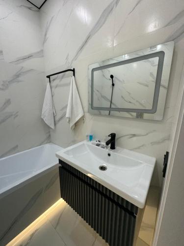 uma casa de banho com um lavatório, um espelho e uma banheira em 1 комнатная квартира посуточно em Taldykolʼ
