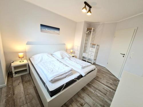 Cette chambre comprend un lit avec des draps blancs et du parquet. dans l'établissement Ferienwohnung Seedune, à Fehmarn