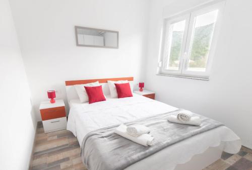 Un dormitorio blanco con una gran cama blanca con almohadas rojas. en House Bartulovic - Jan Apartment with a pool, en Ston