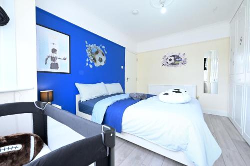 SPACIOUS 5 BEDROOM HOUSE NEXT TO TOTTENHAM STADIUM في لندن: غرفة نوم بحائط ذات لهجة زرقاء وسرير