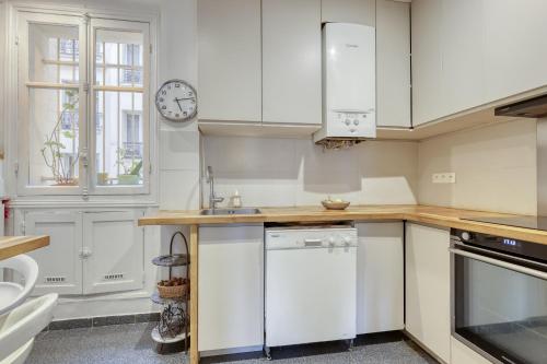 une cuisine avec des placards blancs et une horloge murale dans l'établissement Classic & Charming Parisian flat - Luxury 16th, à Paris