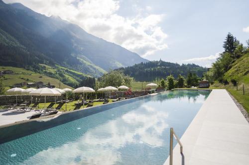 a swimming pool with chairs and umbrellas and mountains at Hotel Sonklarhof in Ridanna